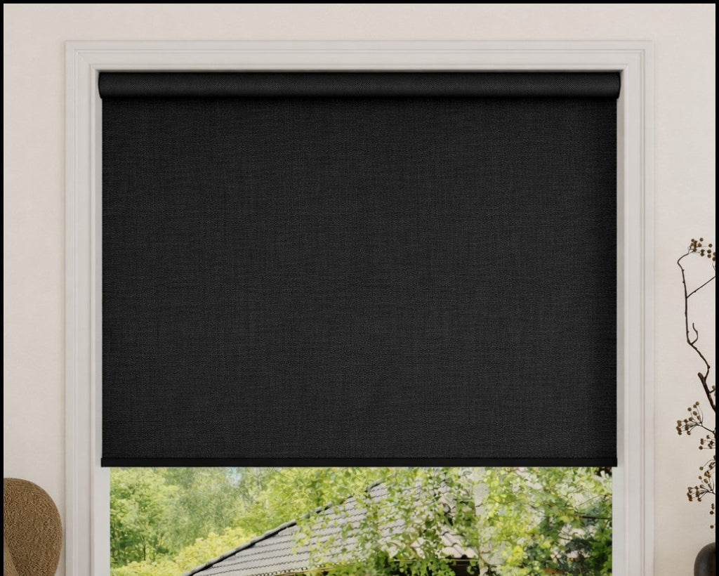 Black roller blind covering a window with a view of greenery outside.